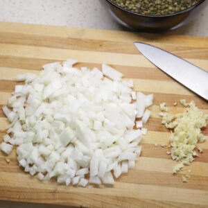 Pile of diced onion on cutting board next to minced garlic and blade.