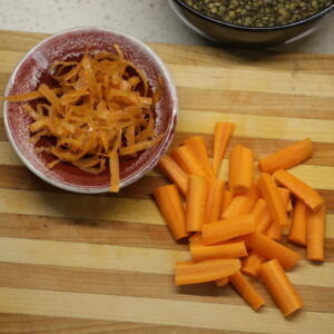 Chopped carrots on a cutting board next to a small bowl of carrot peels.