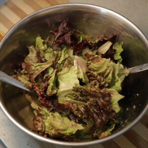 Metal bowl with red leaf lettuce and metal utensils sitting in it.