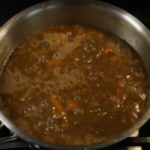 Brown lentil stew with carrots simmering in a pot.