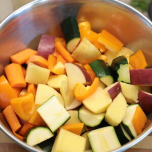 Colorful chunks of vegetables in a steel bowl: zucchini, bell pepper, red skinned potatoes and carrots.