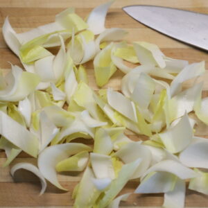 Yellow endive slices next to knife blade on cutting board.