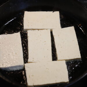 Rectangles of white tofu frying in a cast iron pan.
