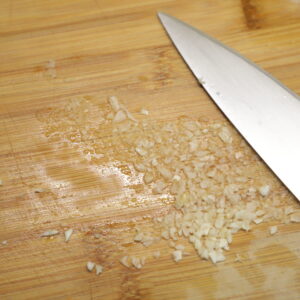 Mashed garlic with knife blade on cutting board.