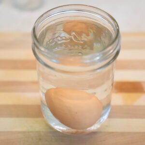 Chicken egg at the bottom of a Mason jar filled with water.