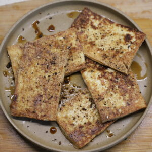 Brown plate with golden seasoned tofu rectangles.