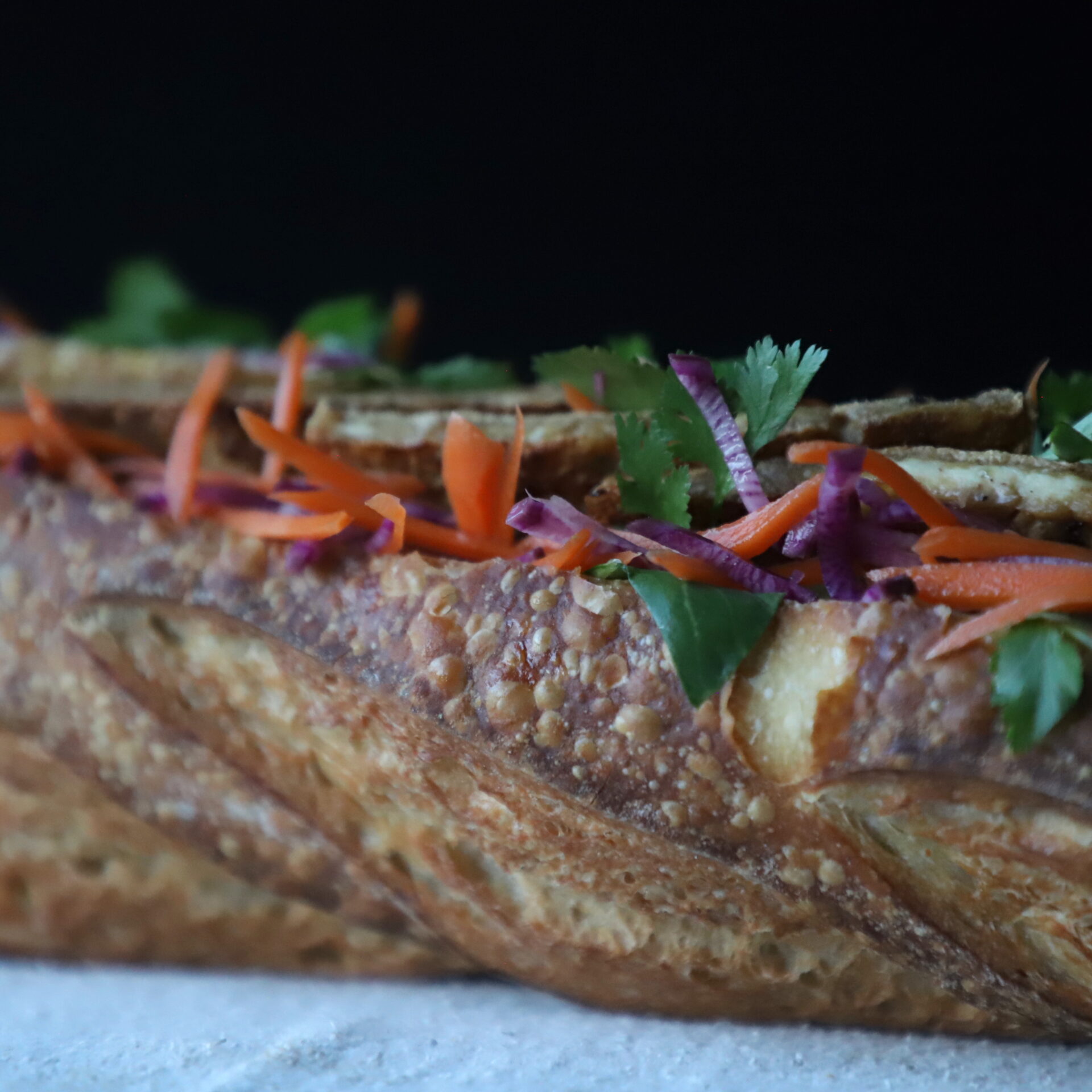 Close up side view of stuffed sourdough banh-mi, on a white cloth and black background.
