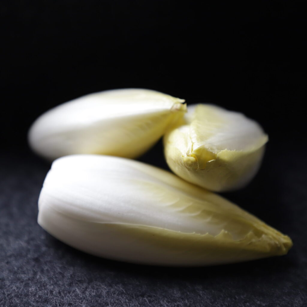3 yellow endive heads poised on each other on a dark gray cloth