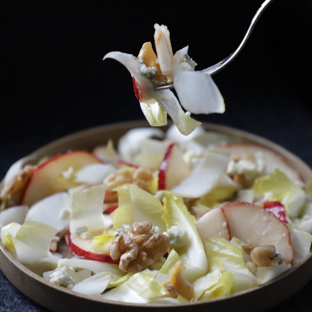 close up view of endive salad plate and a fork lifting a bite in the air