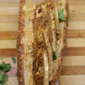 Baguette cut open lengthwise and stuffed with tofu on a cutting board.