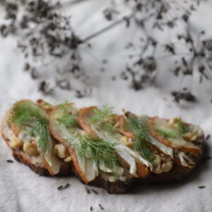 Fennel and Bosc pear toast next to grayish fennel seeds.