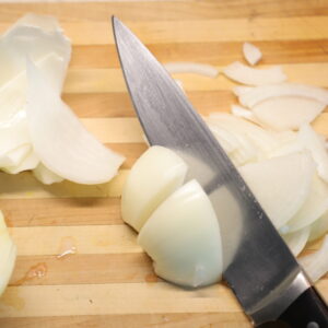 Yellow onion being sliced on a wood cutting board.
