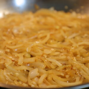 Close up of golden yellow onion slices in a pan.