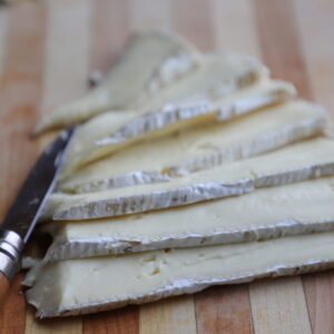 Slices of off-white brie cheese on a cutting board with pocket knife.