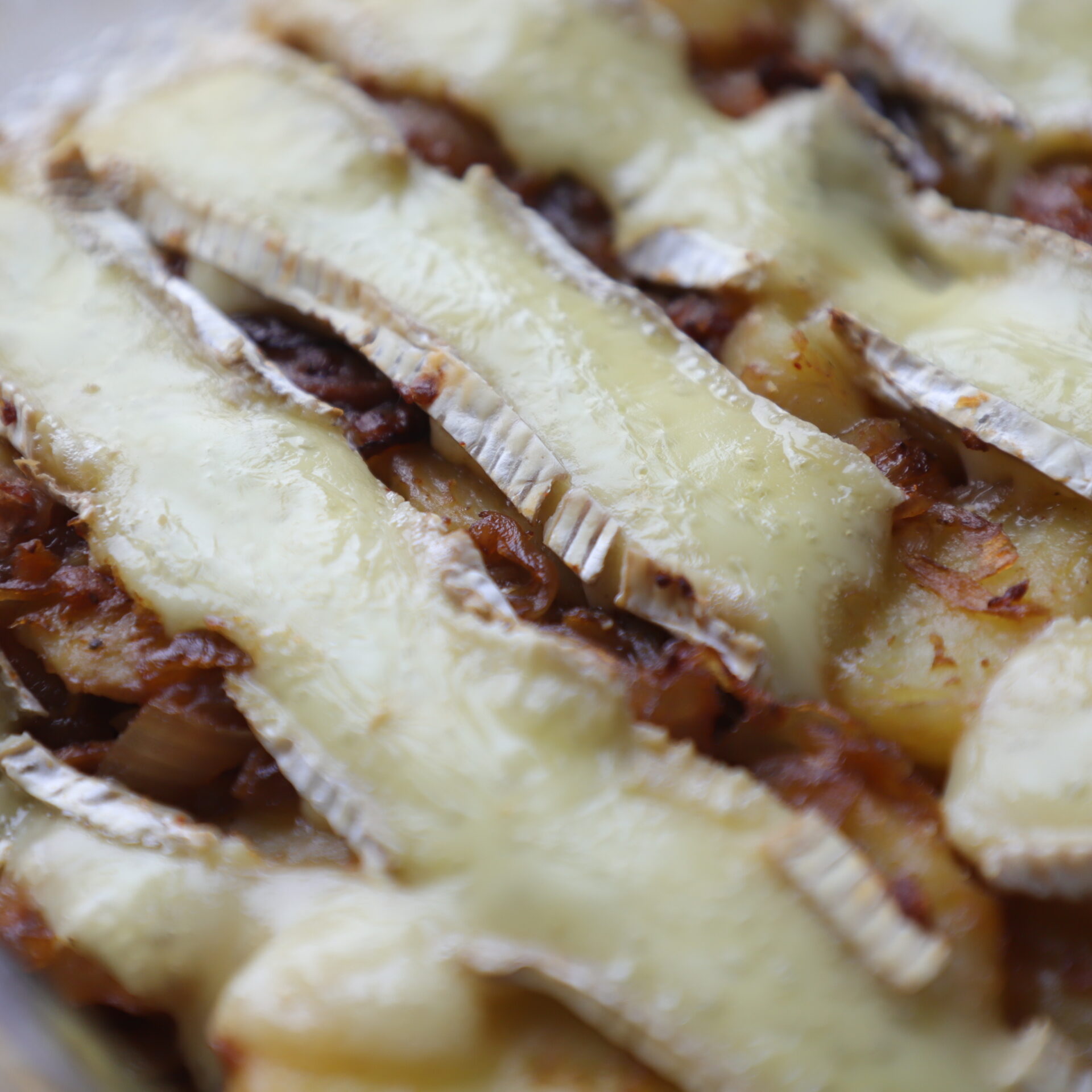 Close up of tartiflette after baking and showing shiny, gooey cheese slices.