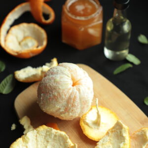 Peeled orange on cutting board with jar of honey and bottle of orange blossom water in the back.