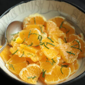 Close up of orange salad in a ceramic white bowl and topped with shreds of fresh mint.