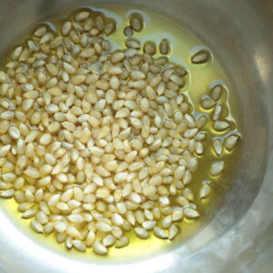 Top view of yellow popping corn in olive oil in a steel pan.