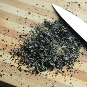 Minced nori seaweed on a cutting board next to a chef's knife.
