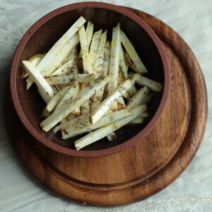 Top view of celeriac sticks in a ceramic bowl on a wooden round cutting board.