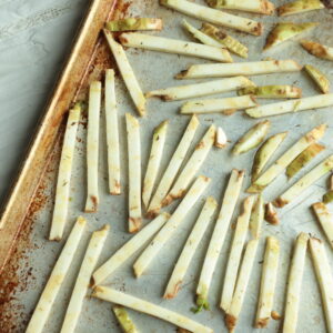 Part of a sheet pan with celeriac fries spaced out on it and not yet baked.