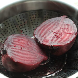 Two cooked beet halves in a steamer basket, still steaming.