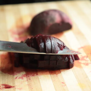 Cooked beet on a wooden cutting board, being sliced horizontally.