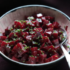 Black-rimmed bowl holding French beet salad garnished with chives, on a dark background.