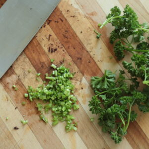 Top view of minced parsley stems next to parsley leaves.