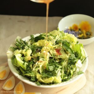 Vinaigrette drizzling on a lush bowl of dandelion salad and quartered boiled eggs on the side.