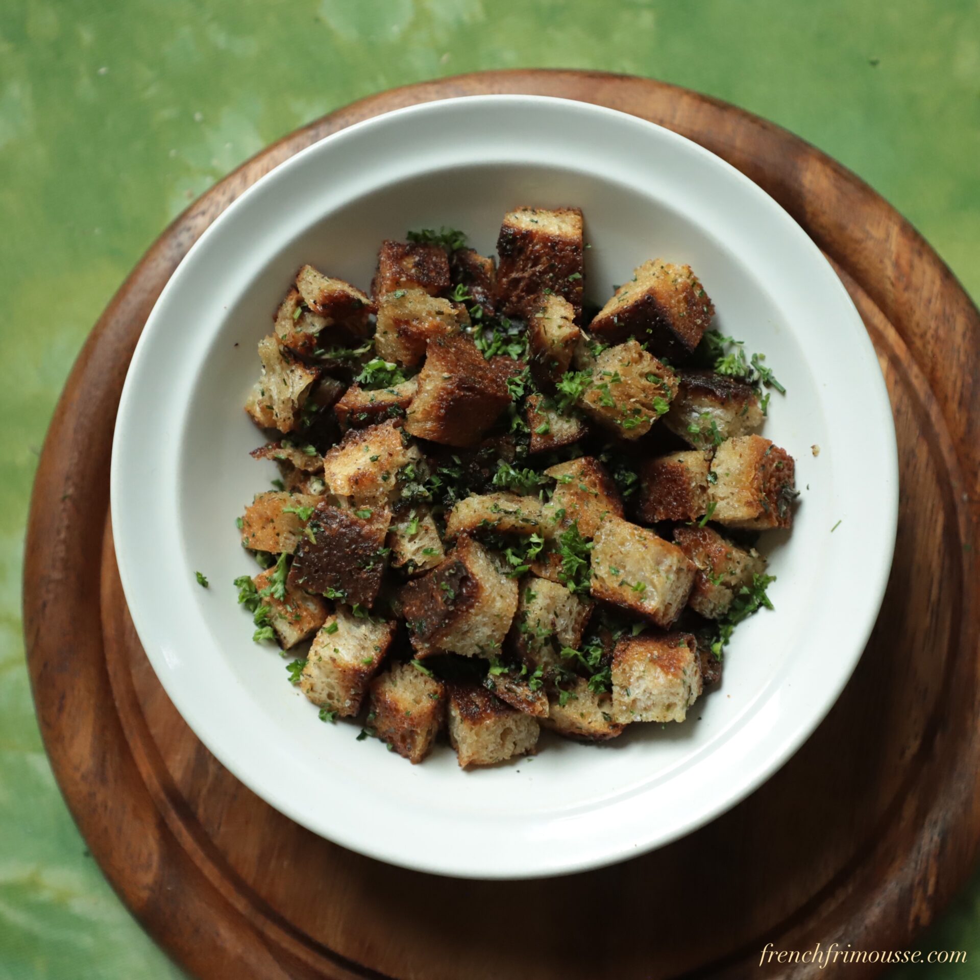Top view of a while bowl filled with toasted bread cubes speckled with herbs.