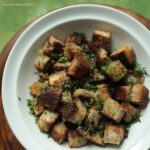 Close up of Garlic and Herbs Croutons in a white bowl and a light green background.