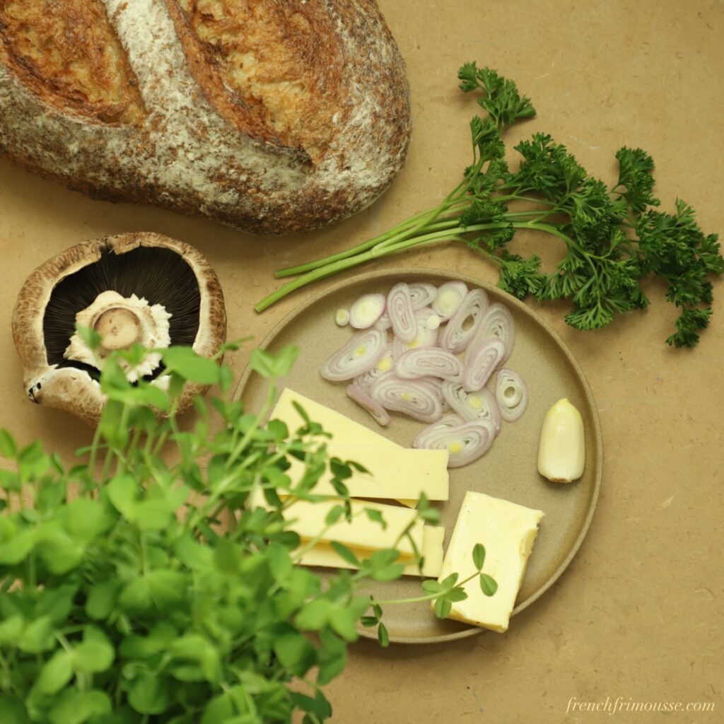 Bird's eye view of bread loaf, parsley, portobello, cheddar, sliced shallots, and pea shoots.