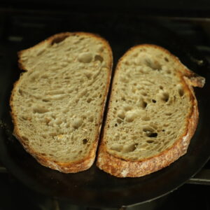 2 sourdough slices being toasted on a comal on the stove.