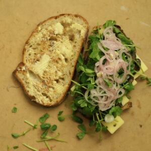 Open Portobello Sandwich filled with pea shoots, shallots, and spread with butter, and just about to be closed.