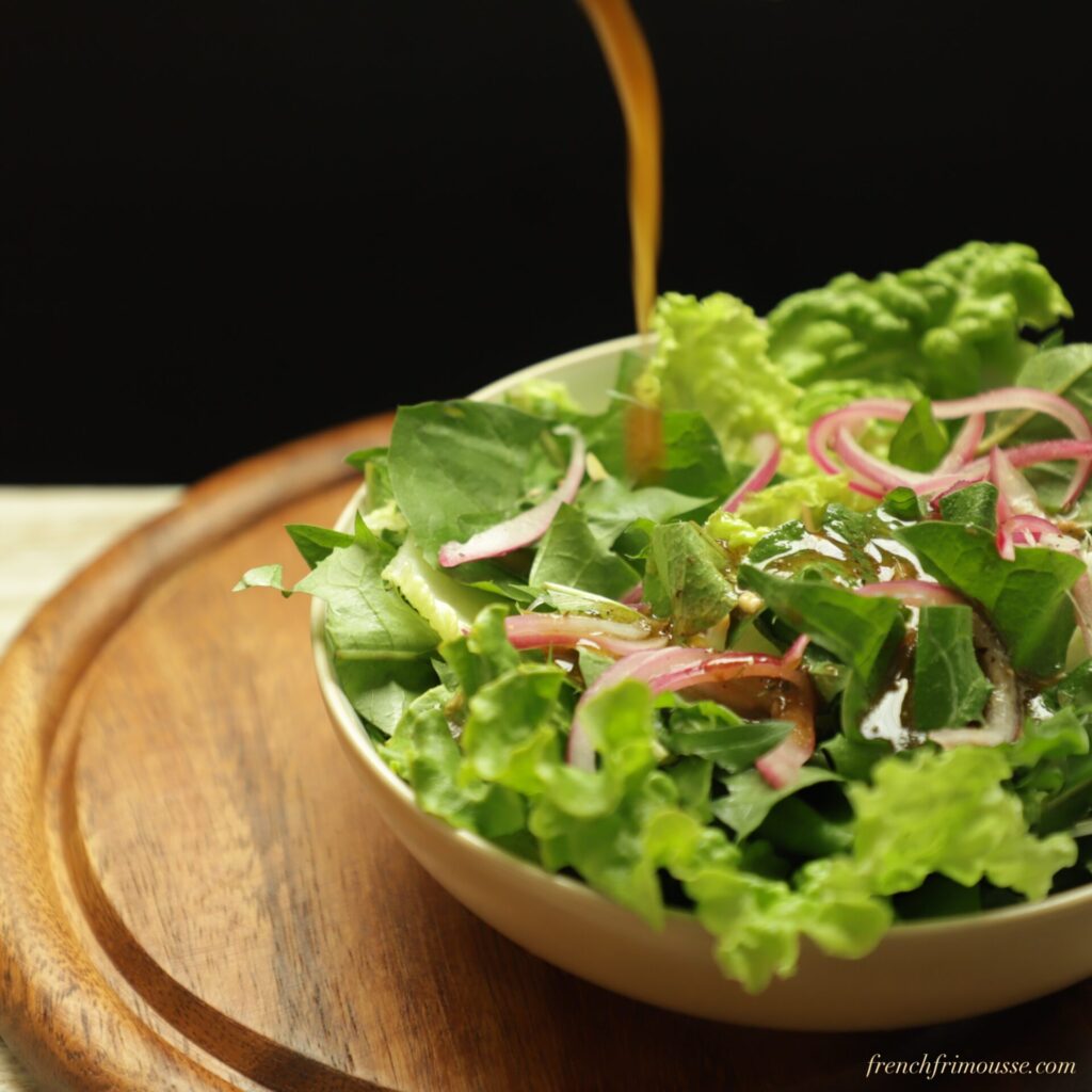 Drizzle of balsamic dressing falling on a bright green bowl of salad with pickled red onion on a black background.